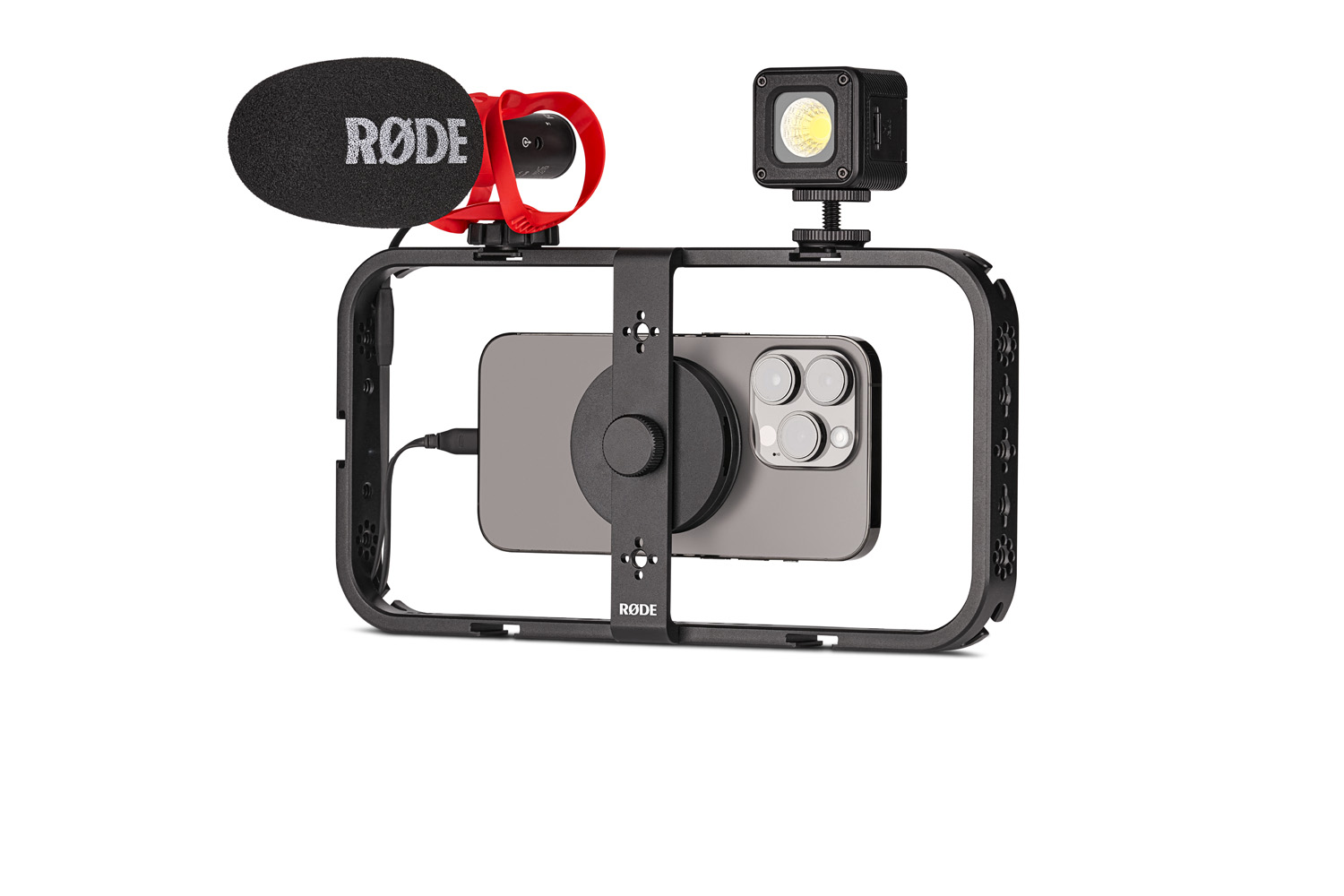 RØDE Phone Cage equipped with a smartphone and various accessories for mobile filmmaking. On the left, a foam-covered RØDE microphone with a red coiled cable, and on the right, a compact LED light panel. The setup is designed to be a comprehensive mobile recording solution, mounted on a black frame surrounding the phone