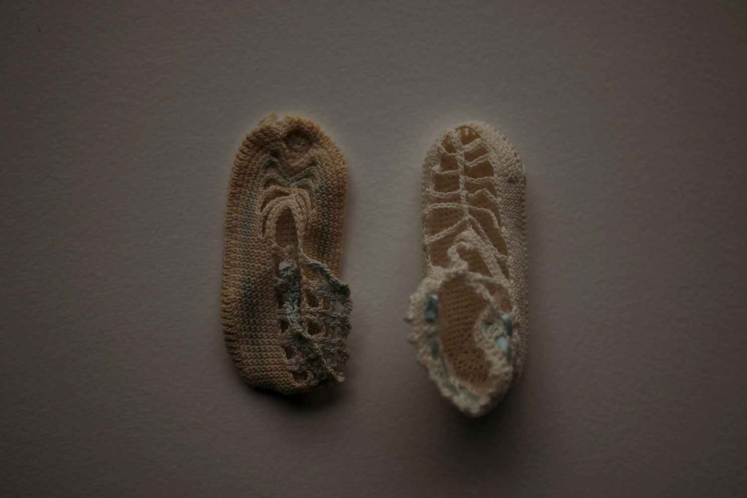 Two heavily worn, hole-ridden knitted slipper socks lie on a flat grey surface, highlighting their textured details and signs of wear.