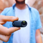 Man holding thumb-sized Insta360 camera between his thumb and forwfinger