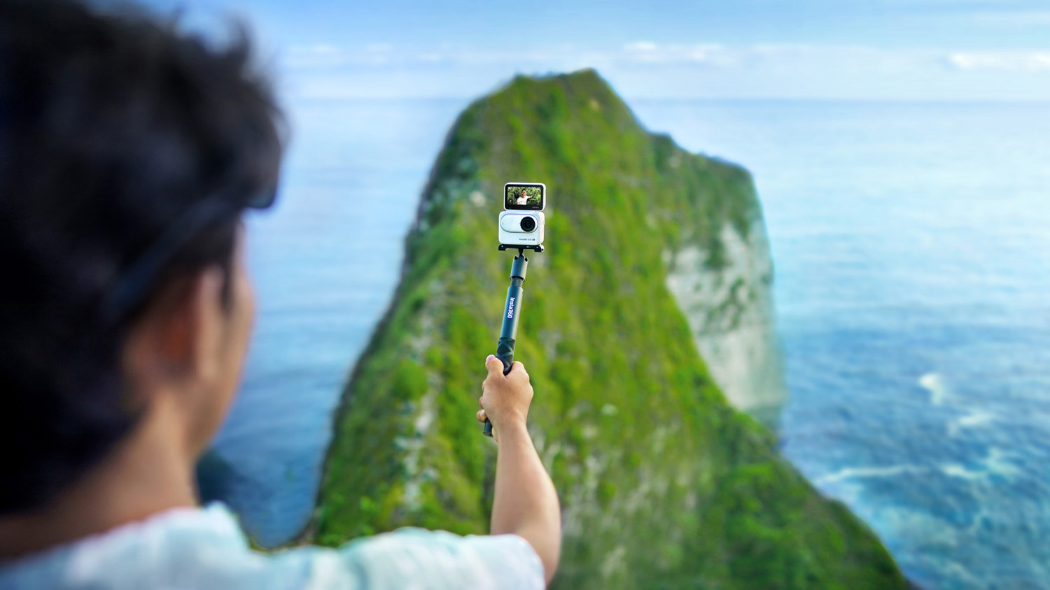 Person holding Insta 360 GO 3S camera on the end of a selfie stick while walking along a coastal ridge