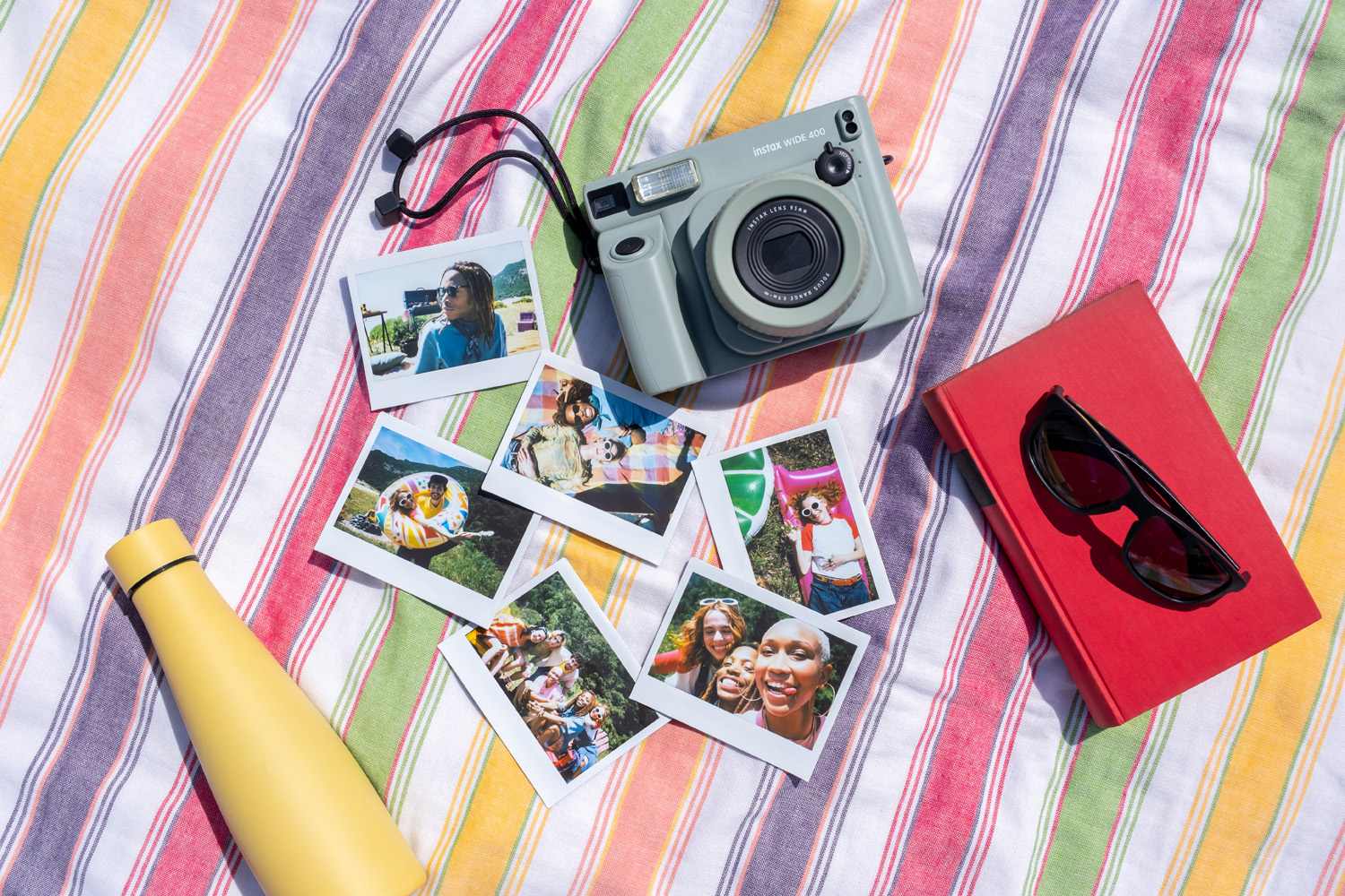 Flatlay of Instax wide 400 camera and a collection of prints on a colourfully striped tablecloth