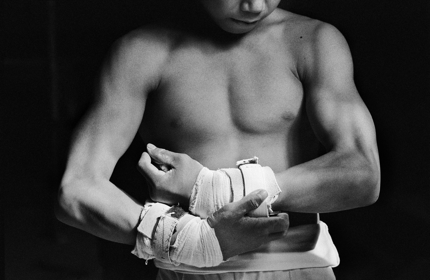 Black and white photo of a young male gymnast in China, adjusting the bandages on his hands with a focused expression, highlighting strength and dedication.